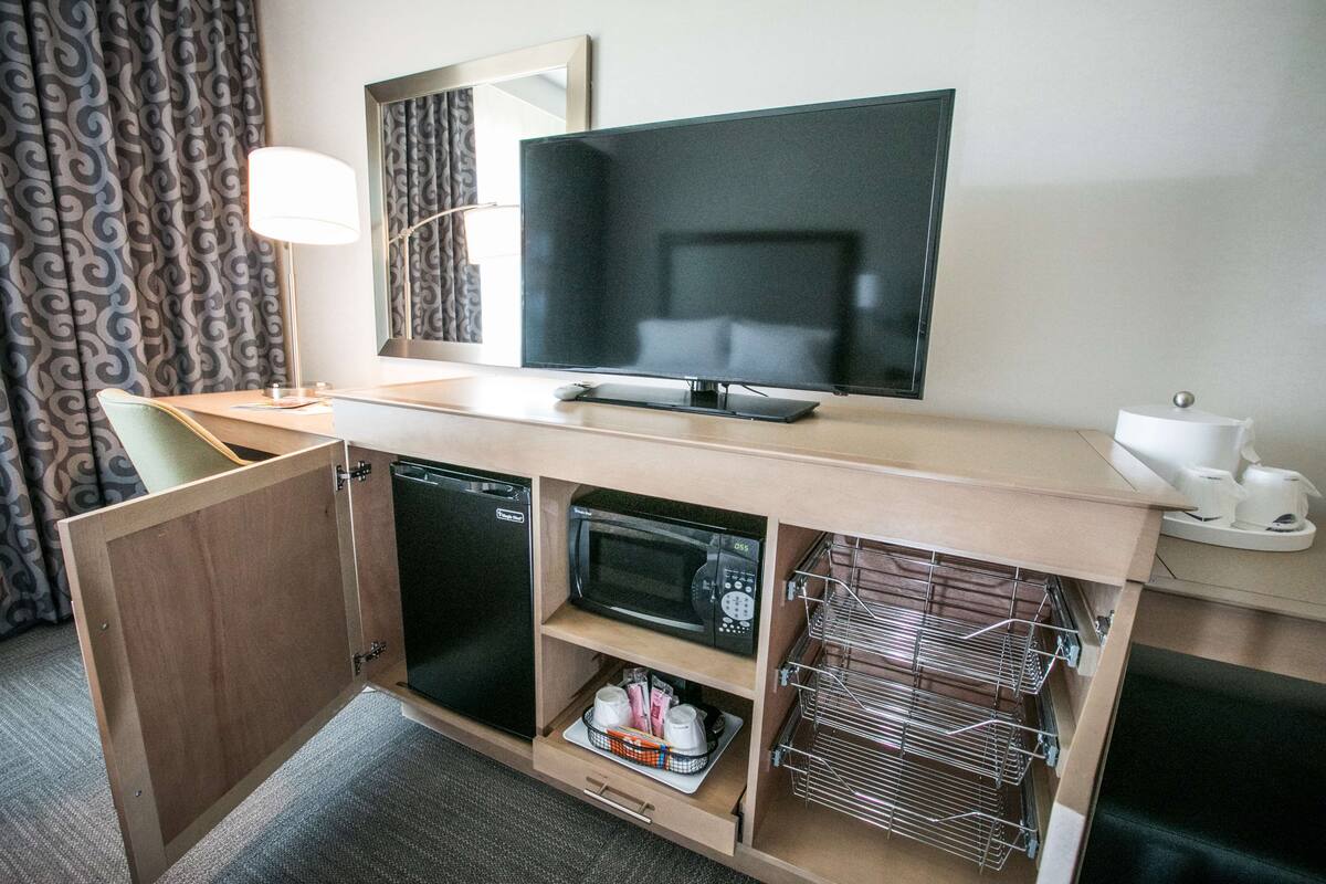 A compact hotel room with a kitchenette, a flat-screen TV, a microwave, a refrigerator, and a small seating area.