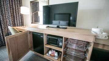 A compact hotel room with a kitchenette, a flat-screen TV, a microwave, a refrigerator, and a small seating area.