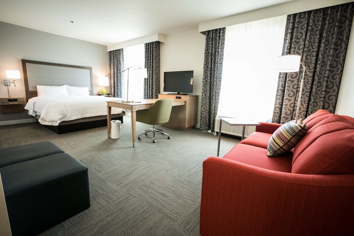 A hotel room with a bed, desk, chair, and red sofa.