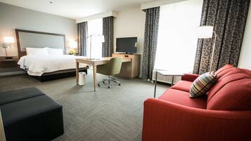 A hotel room with a bed, desk, chair, and red sofa.