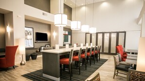 A hotel lobby with a long reception desk, multiple seating areas, and a large flat-screen TV mounted on the wall.