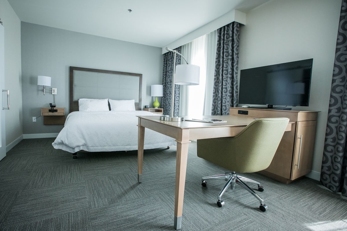 A hotel room with a bed, desk, chair, television, and curtains.