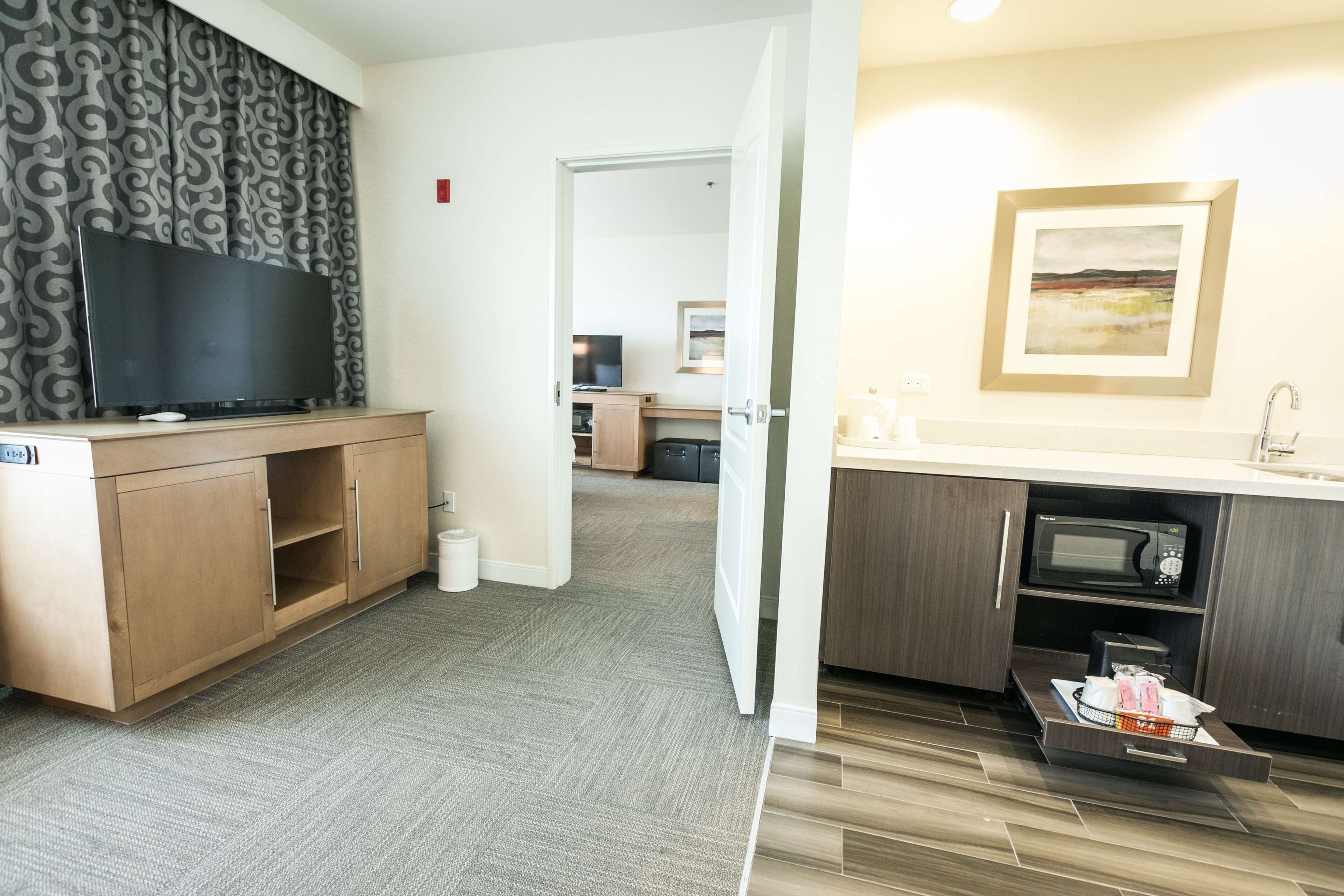 Ein modernes Hotelzimmer mit Flachbildfernseher, Holzschränken, einer Mikrowelle und einem Waschbecken.