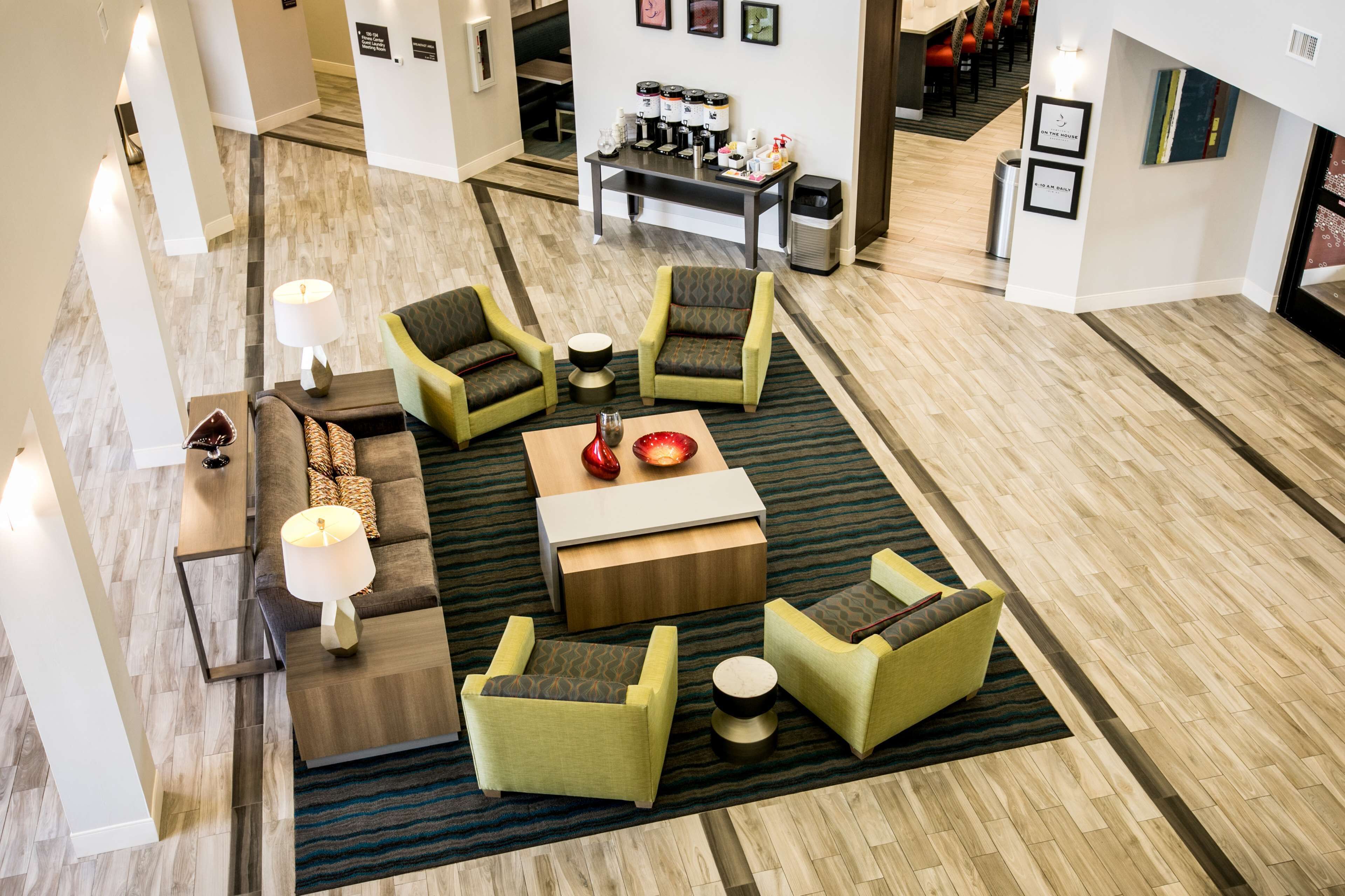 A modern hotel lobby with a seating area featuring green armchairs, a sofa, and a coffee station.