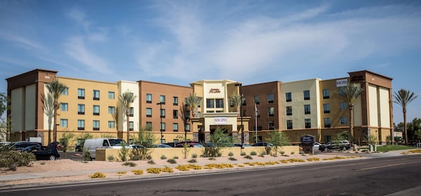 A multi-story hotel with a beige and brown facade, multiple windows, and a sign indicating it is now open.