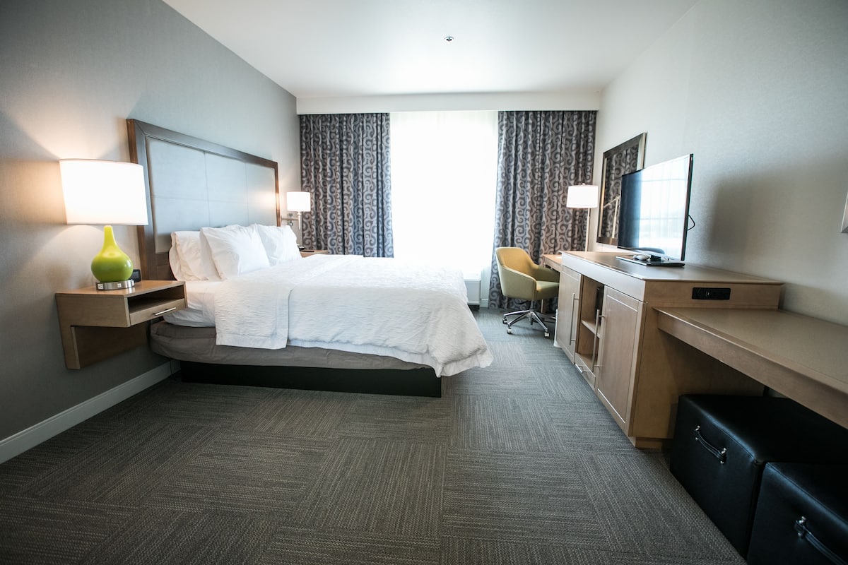 A hotel room with a bed, desk, chair, TV, and curtains.