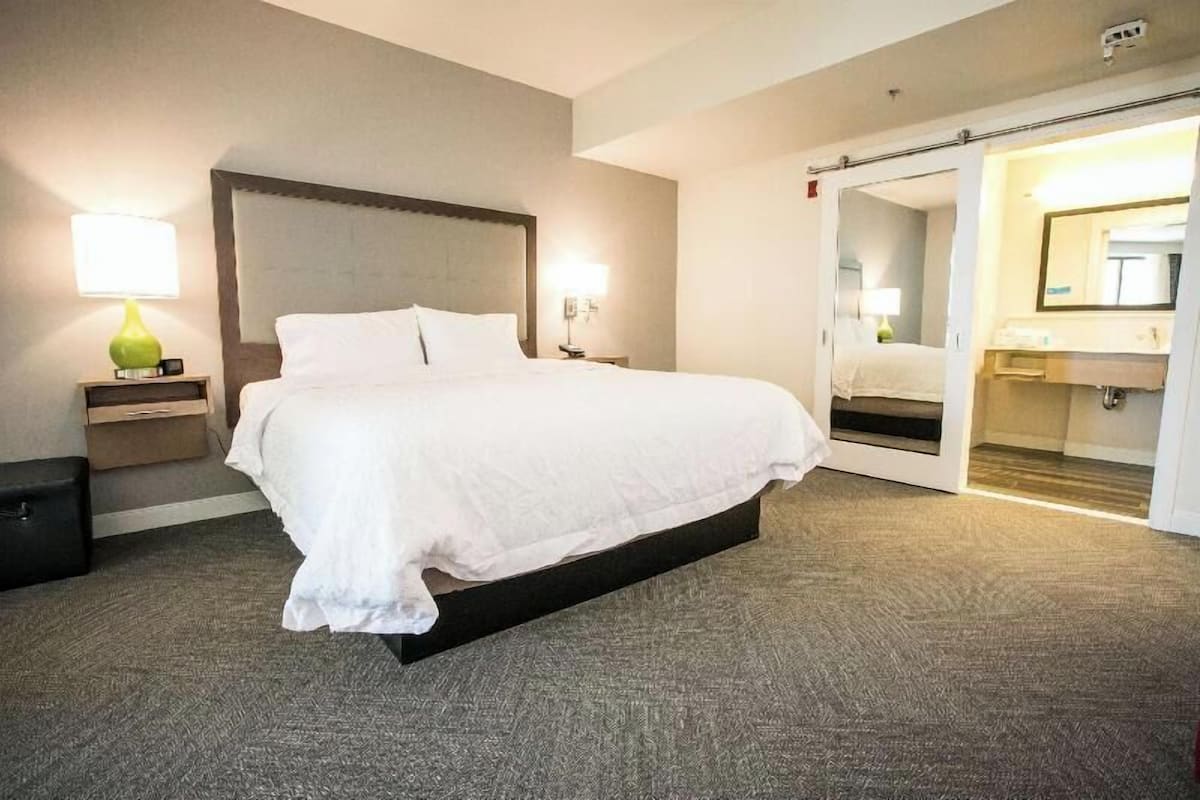 A hotel room with a bed, bedside lamps, a mirror, and a sliding door to a bathroom.