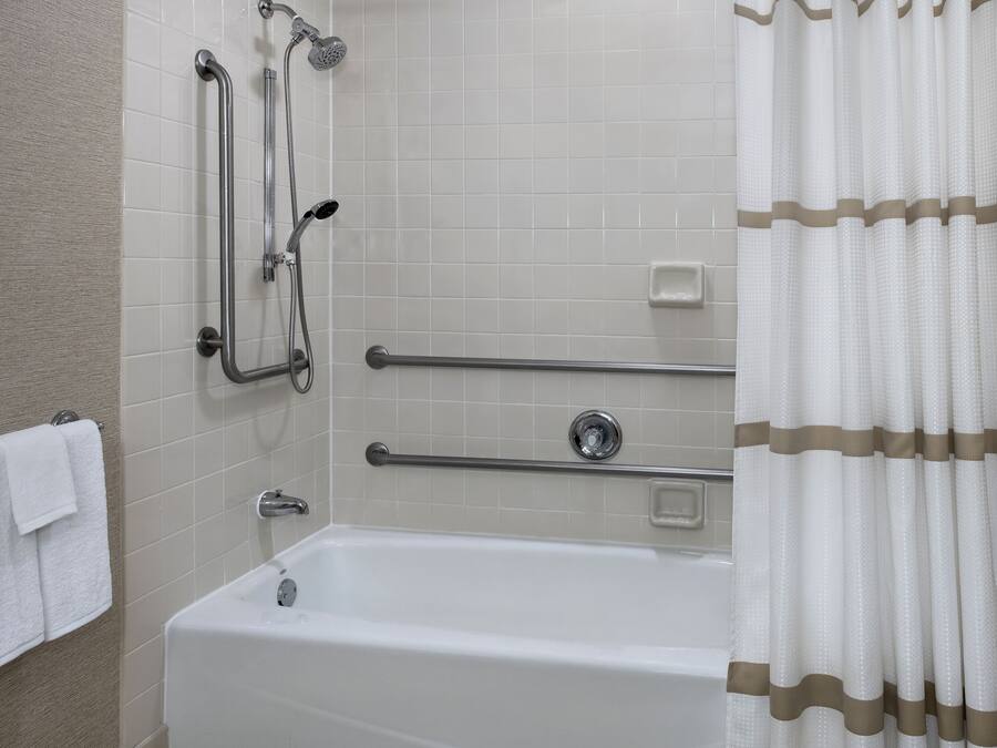 A bathroom with a bathtub, grab bars, a shower head, and a curtain.