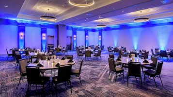 A large conference room with multiple tables and chairs, arranged in a U-shape, with blue ambient lighting and a carpeted floor.