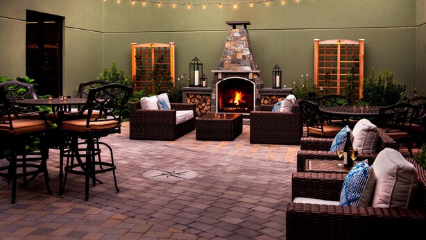 Un patio exterior con mobiliario de mimbre, una chimenea de piedra y luces colgantes.