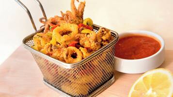 A basket of fried calamari with a side of marinara sauce and a lemon wedge.