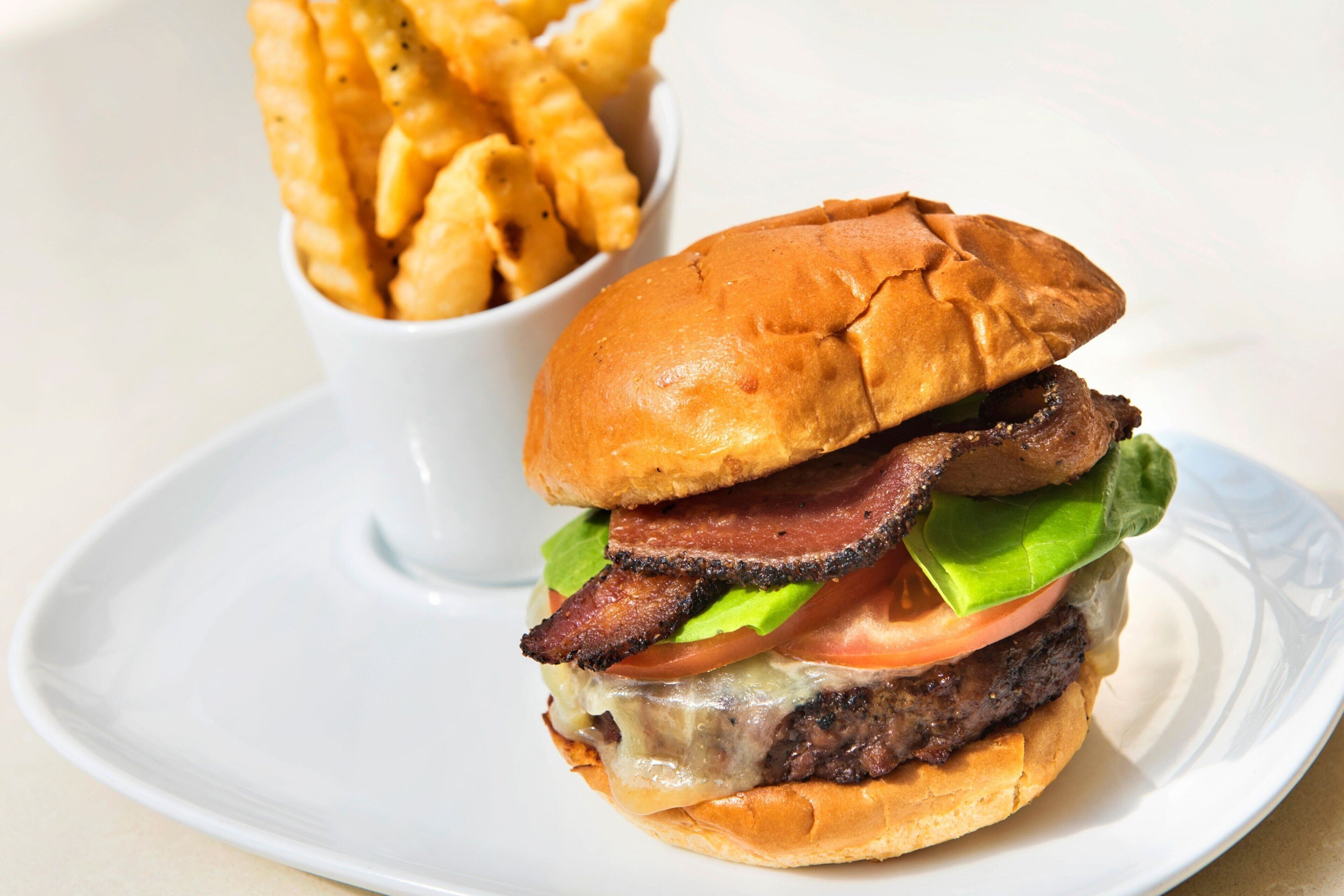 Hamburguesa con tocino, lechuga, tomate y queso, acompañada de papas fritas.