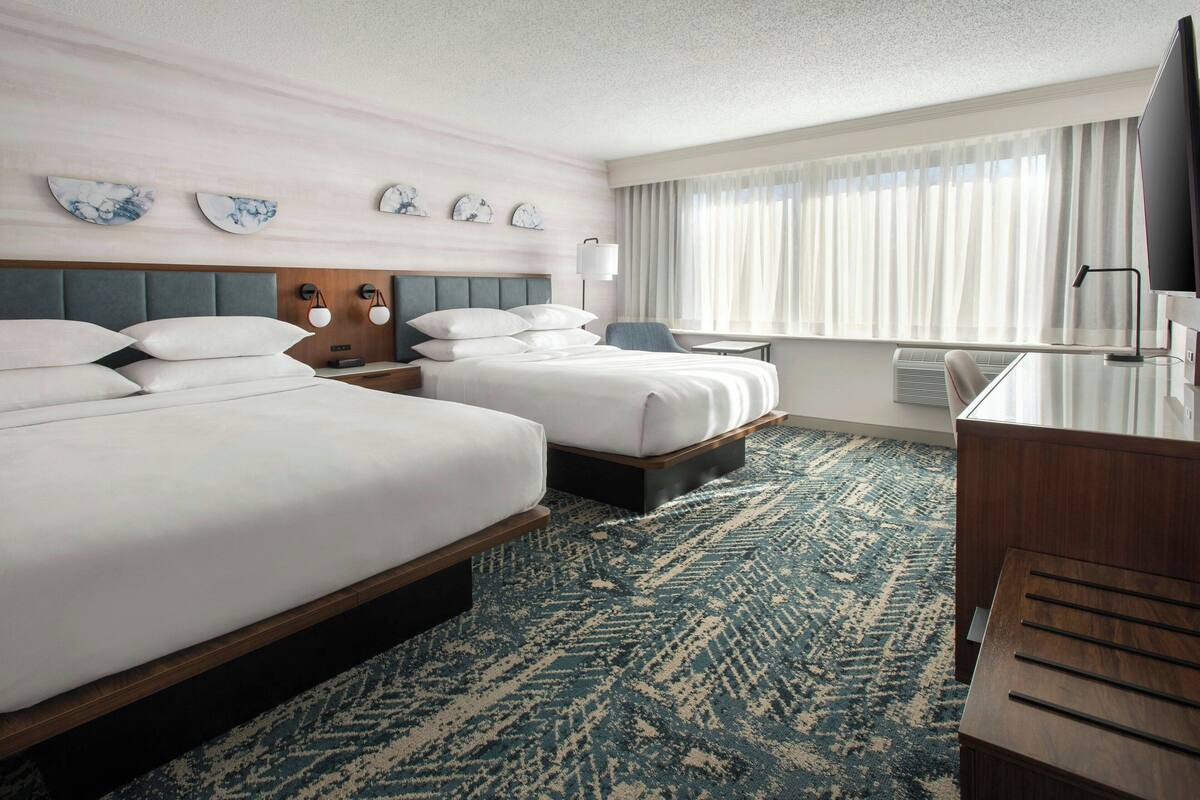 A hotel room with two beds, a desk, a chair, a TV, and a window with curtains.