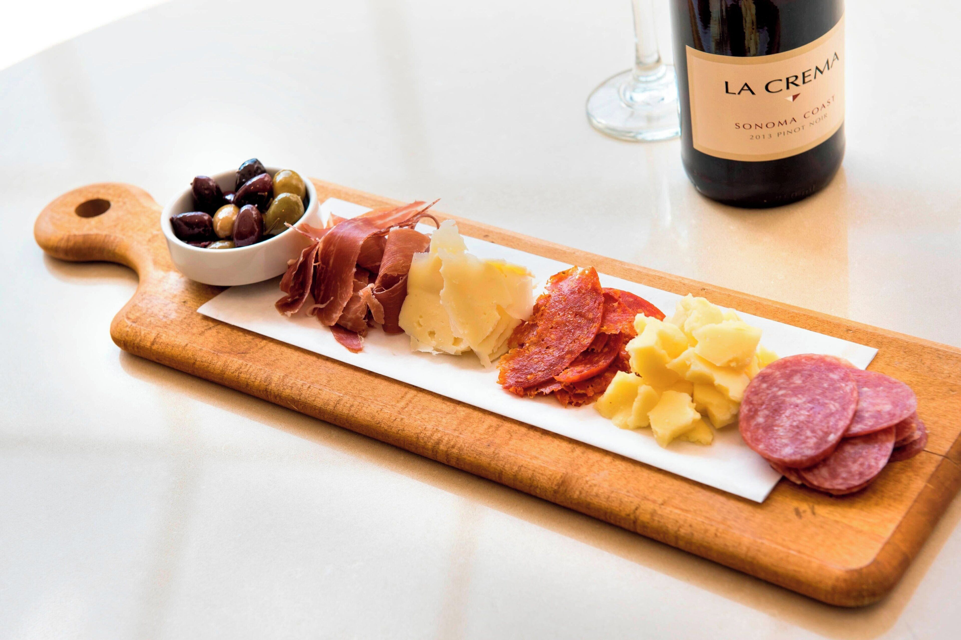 A wooden board with various cured meats, cheese, and olives, accompanied by a bottle of wine.
