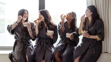 Cuatro personas vestidas de oscuro sentadas junto a una ventana, cada una sosteniendo un cuenco de comida.