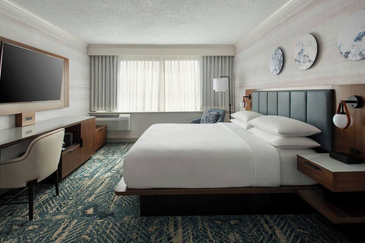 A hotel room with a bed, a desk, a TV, a lamp, and a window with curtains.