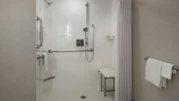A shower with a glass door, a handrail, a showerhead, a handheld showerhead, a towel rack, and a white chair.