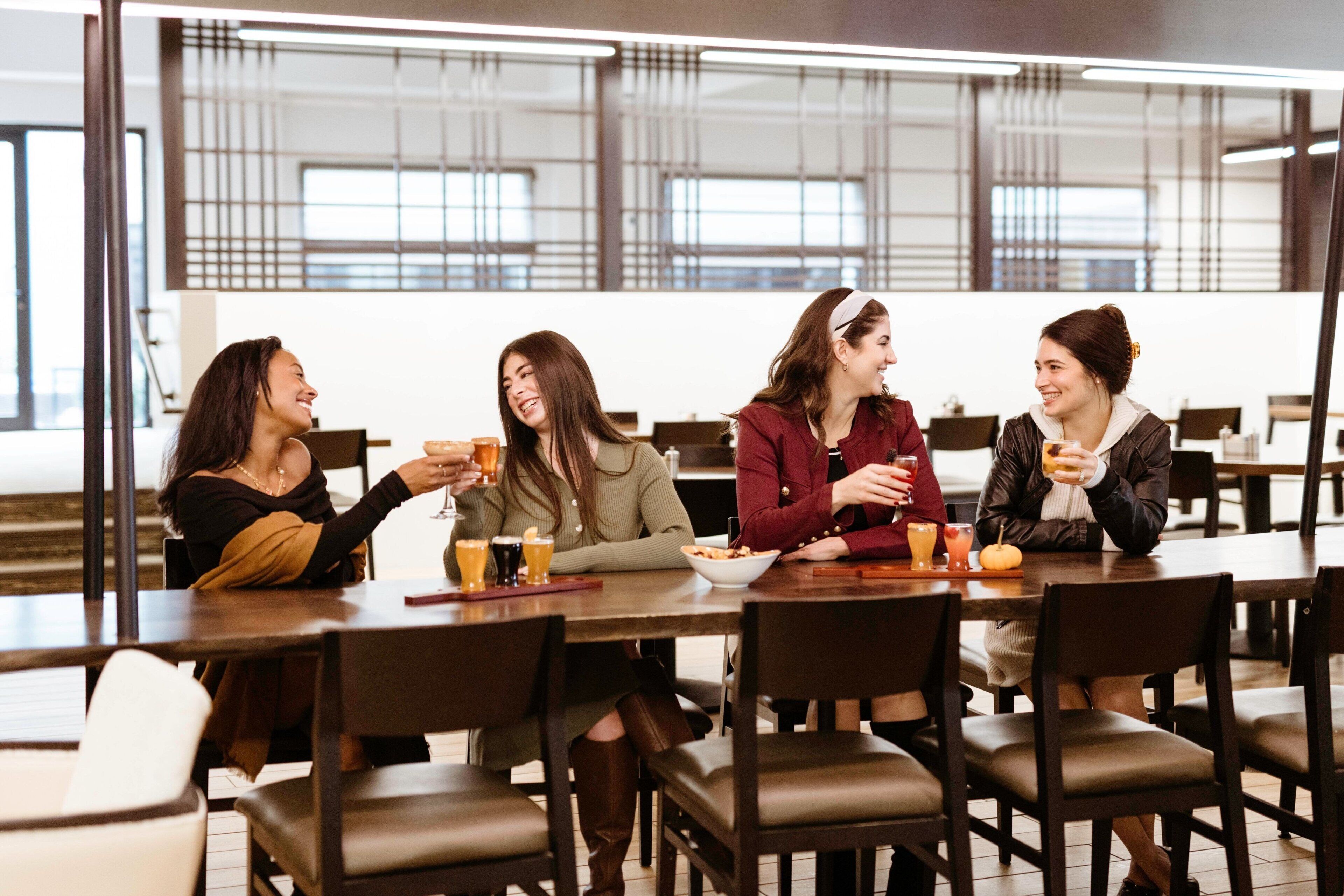 Four people seated at a table in a modern dining area with large windows and a high ceiling.
