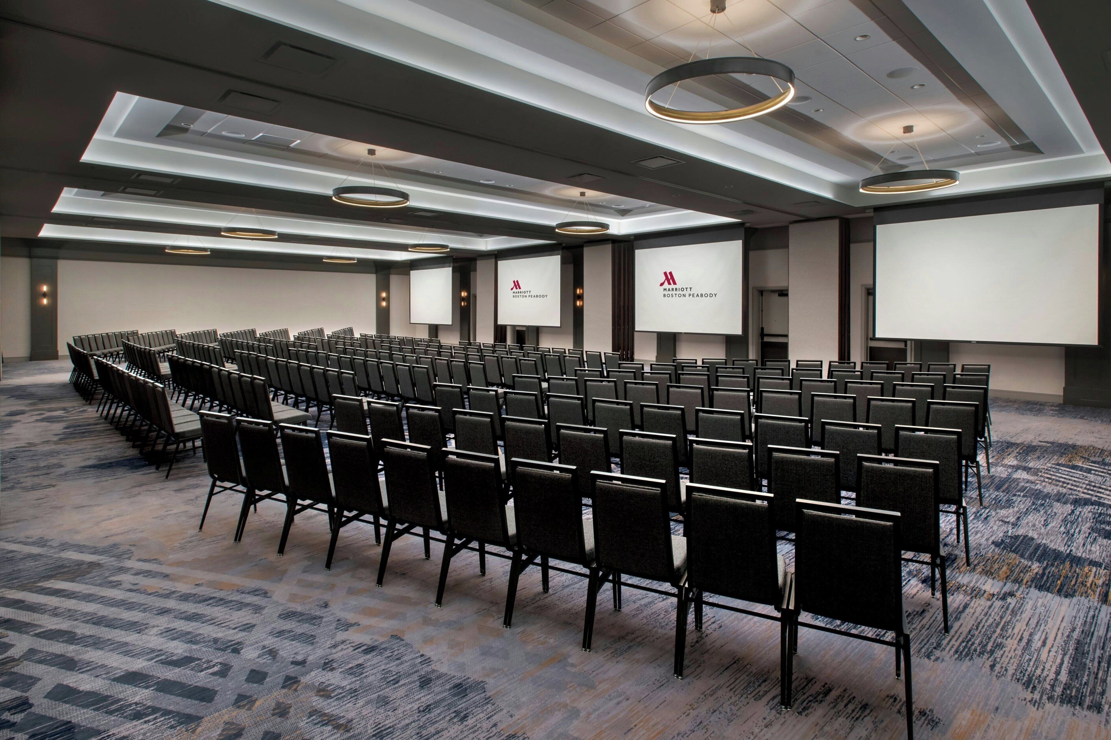 Una sala de conferencias con filas de sillas, una pantalla grande y suelo alfombrado.