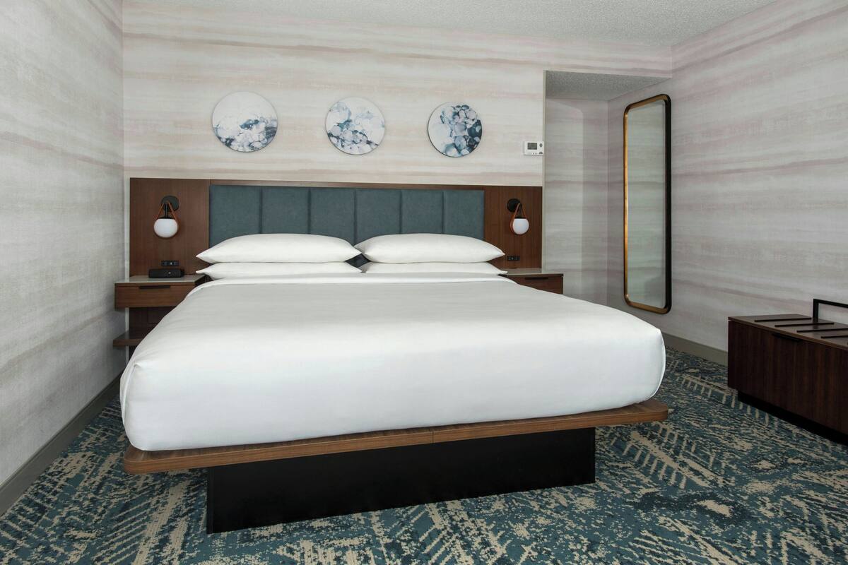 A hotel room with a large bed, a headboard, bedside tables, a mirror, and wall art.