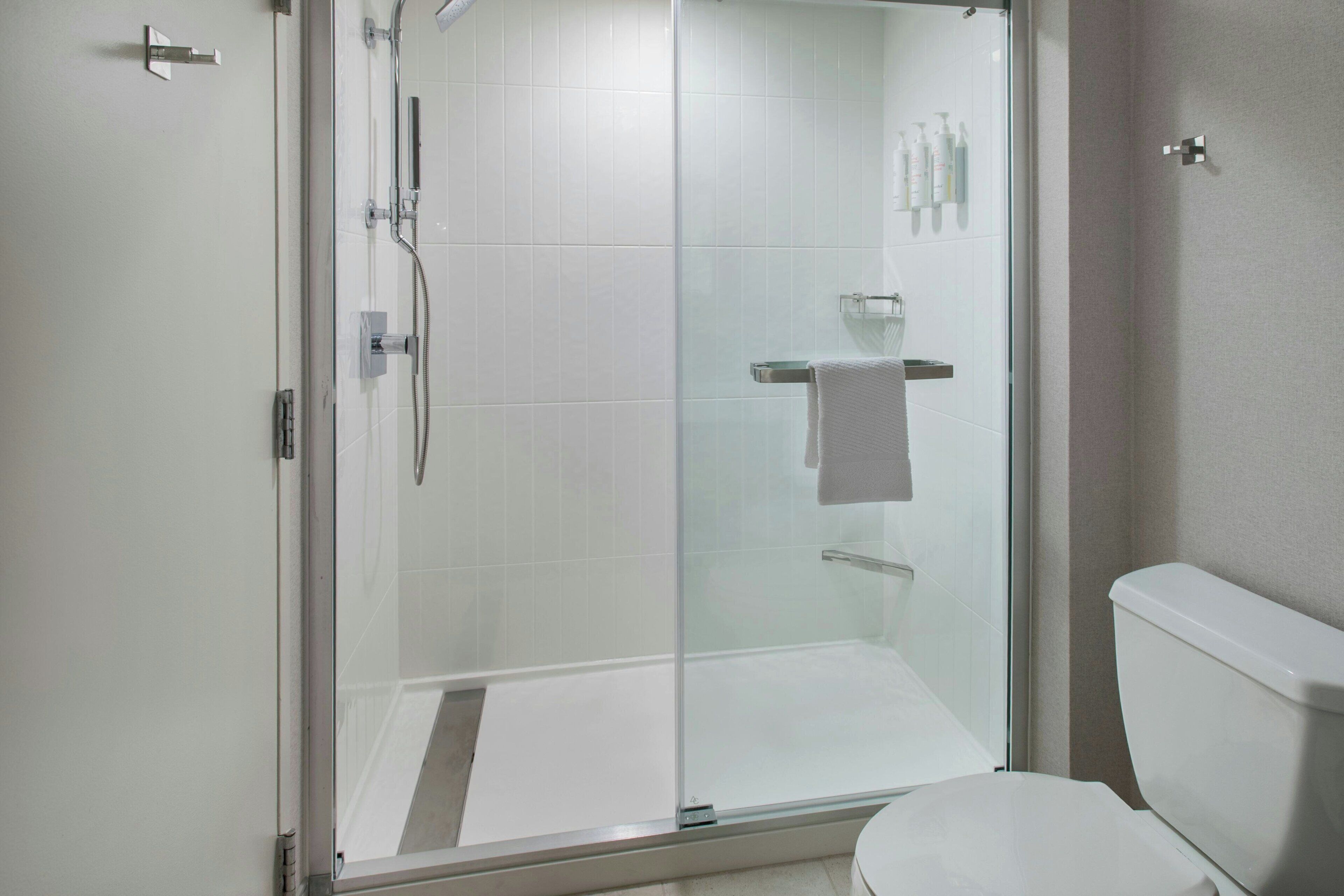 Un baño con ducha envuelta en vidrio, inodoro blanco y puerta de vidrio para la ducha.