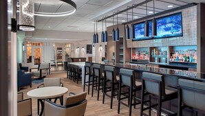 Zona de bar moderna con diversas opciones de asientos, incluyendo taburetes y mesas redondas, y un televisor montado en la pared.