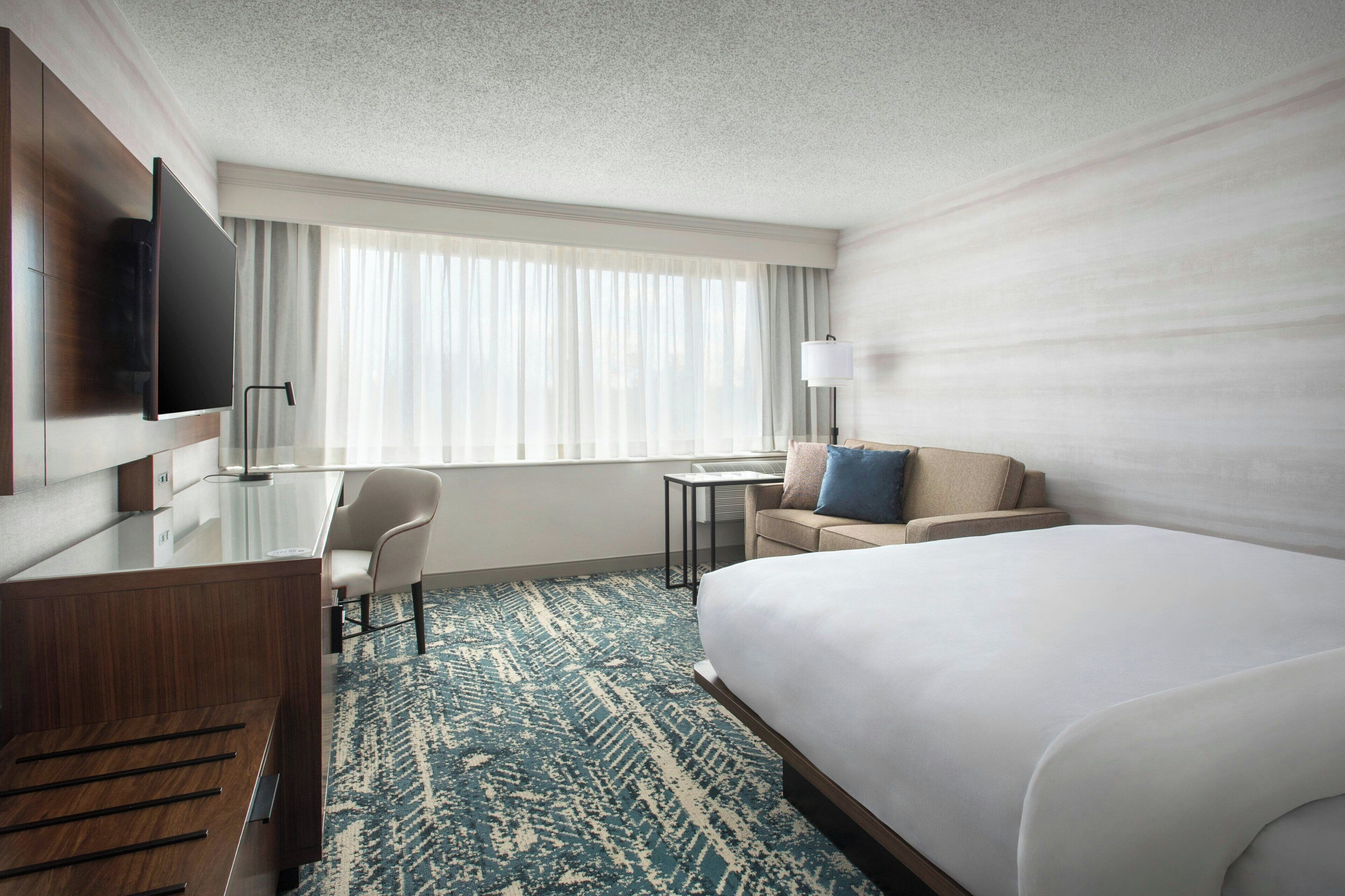 A hotel room with a bed, a desk, a chair, a TV, and a window with curtains.
