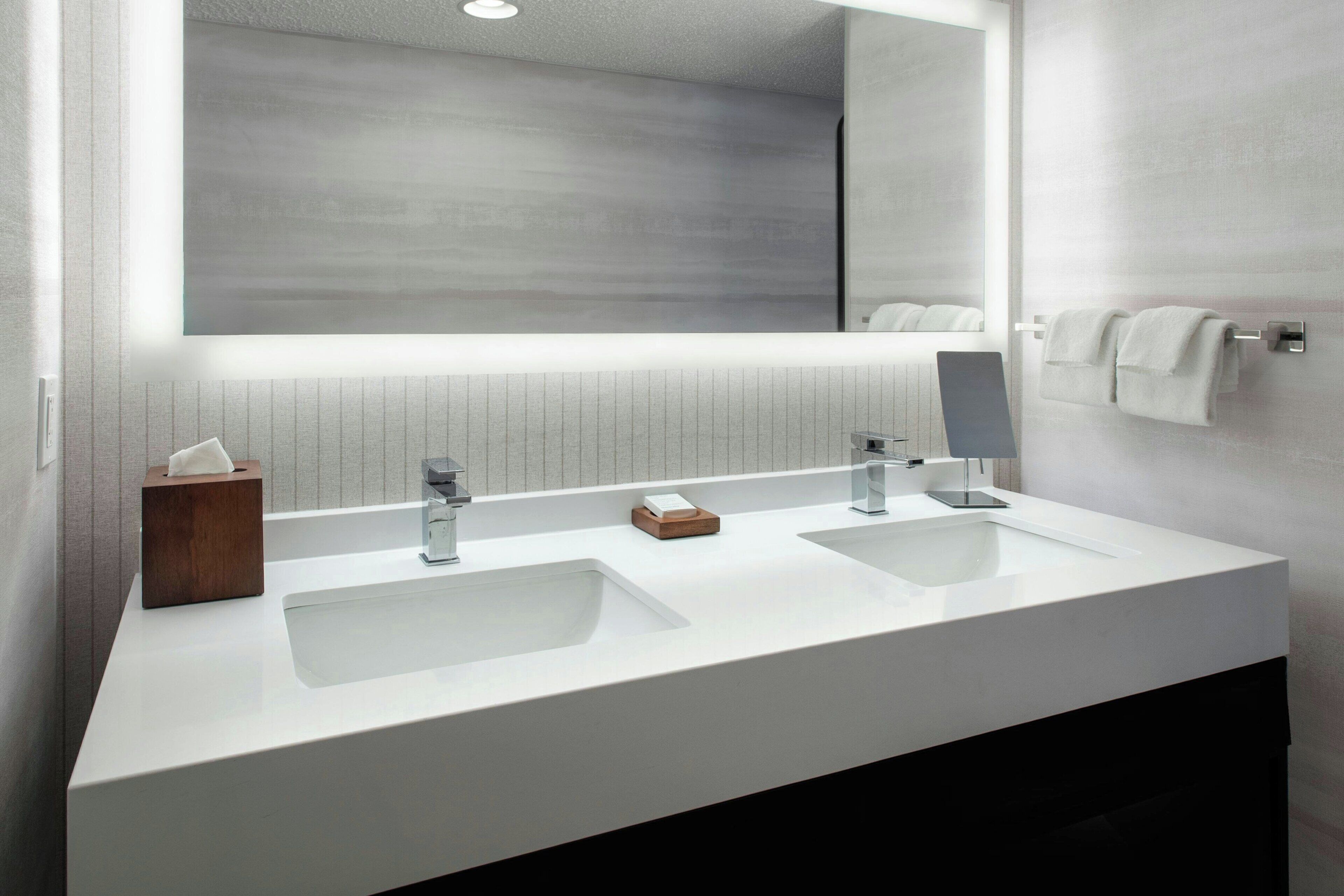 A modern bathroom with two sinks, a large mirror, and a towel rack.