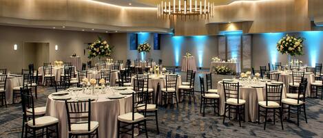 A spacious banquet hall with round tables, chairs, and floral centerpieces.