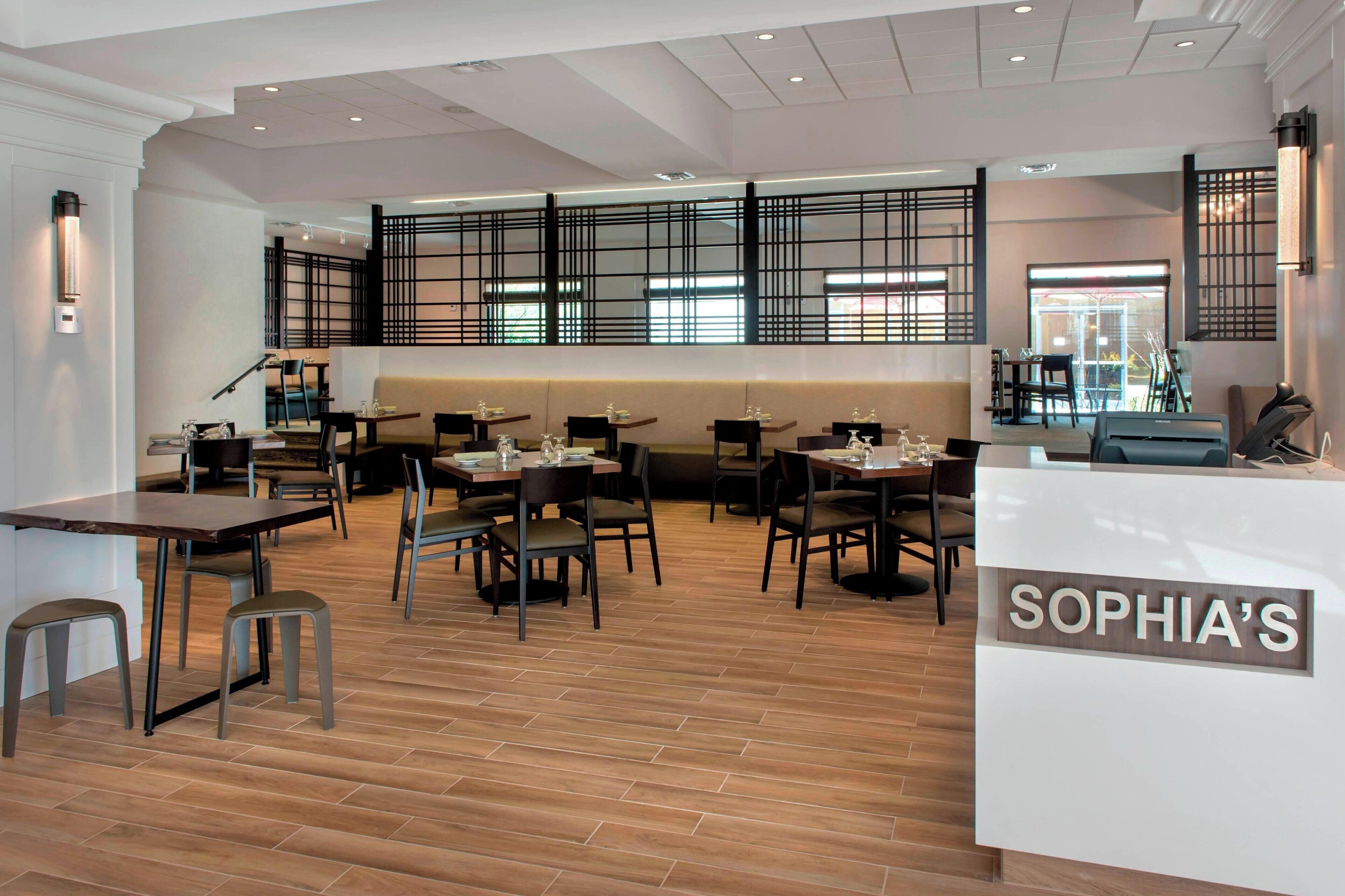 L’intérieur d’un restaurant présente un plancher en bois, plusieurs tables et chaises. On y trouve un comptoir d’accueil portant l’inscription « SOPHIA’S » et un coin salon avec un canapé.