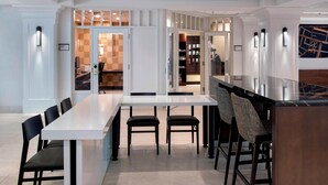 Un comedor de hotel moderno con una larga mesa blanca, sillas negras y una zona de bar con taburetes.