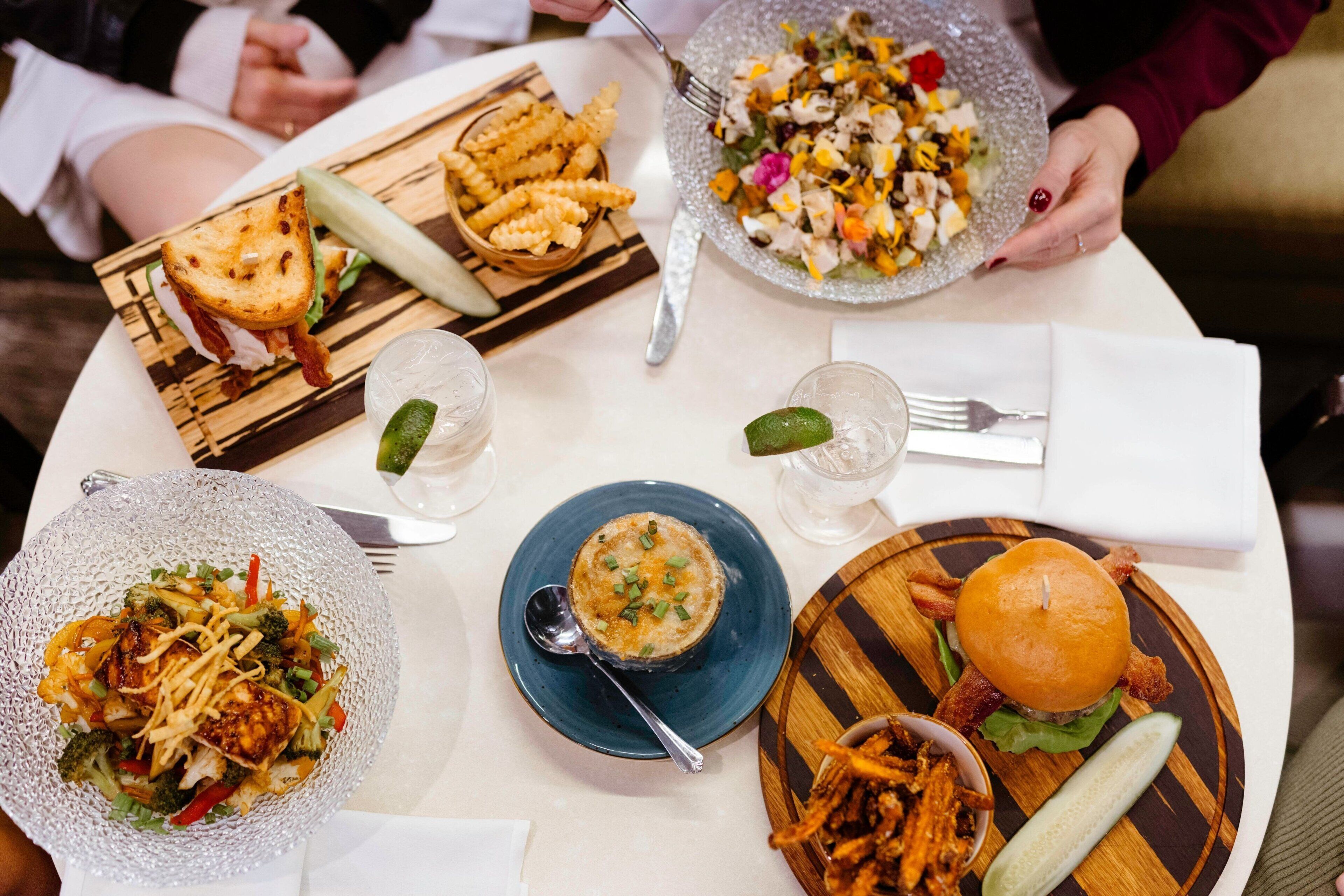A table with various dishes including a burger, a salad, and a bowl of soup.