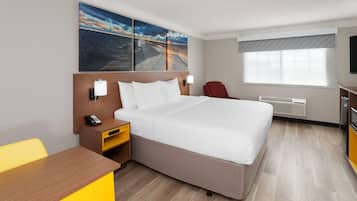 A hotel room with a large bed, a desk, a chair, a TV, and artwork on the wall.