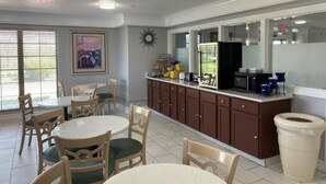 A kitchen with a dining area, a refrigerator, and a trash can. - Days Inn & Suites by Wyndham Arlington Heights (Arlington Heights)