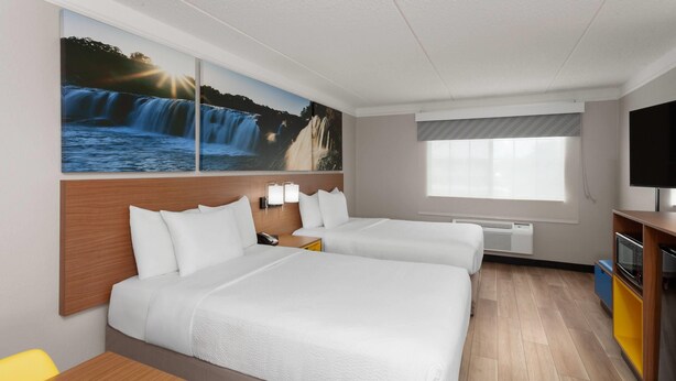 A hotel room with two beds, a TV, a window with blinds, a painting of a waterfall, and a small table. - Days Inn & Suites by Wyndham Arlington Heights (Arlington Heights)