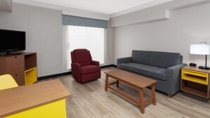 A modern living room with a sofa, armchair, coffee table, TV, and a small table with a lamp. - Days Inn & Suites by Wyndham Arlington Heights (Arlington Heights)