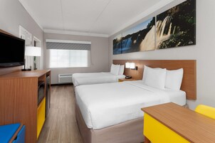 Una habitación de hotel con dos camas, televisión, escritorio y ventana con persianas.
