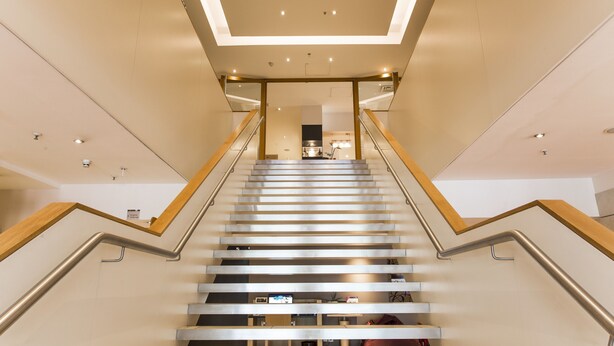 Eine moderne Treppe mit Holzwangen und einer Glaseinfassung, die zu einem hellen Innenraum führt.