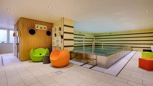 Ein moderner Poolbereich im Innenbereich mit Holzwand, bunten Sitzgelegenheiten und gefliestem Boden.