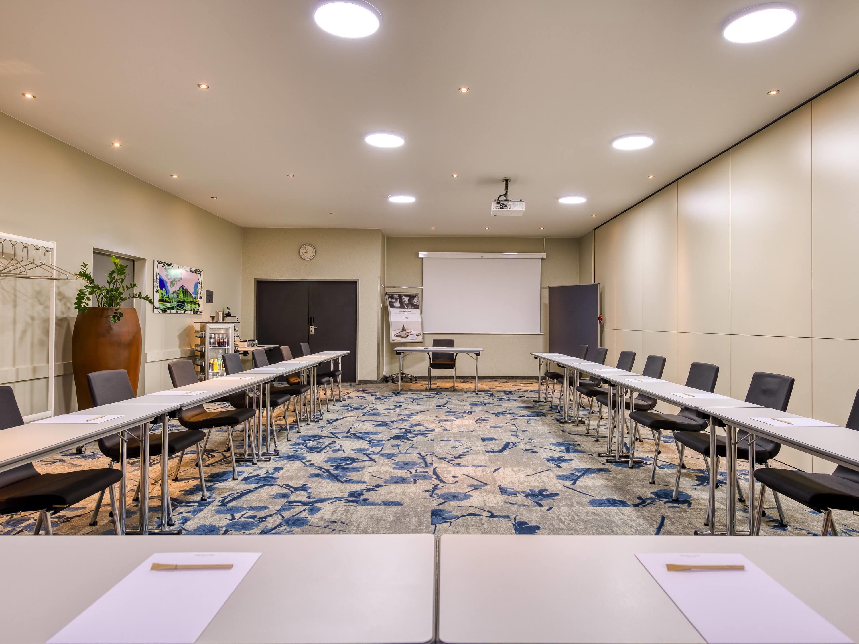 A conference room with a long table, chairs, a projector screen, and a clock on the wall.
