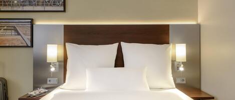 A hotel room with a neatly made bed, two bedside lamps, a headboard, and a framed picture on the wall.