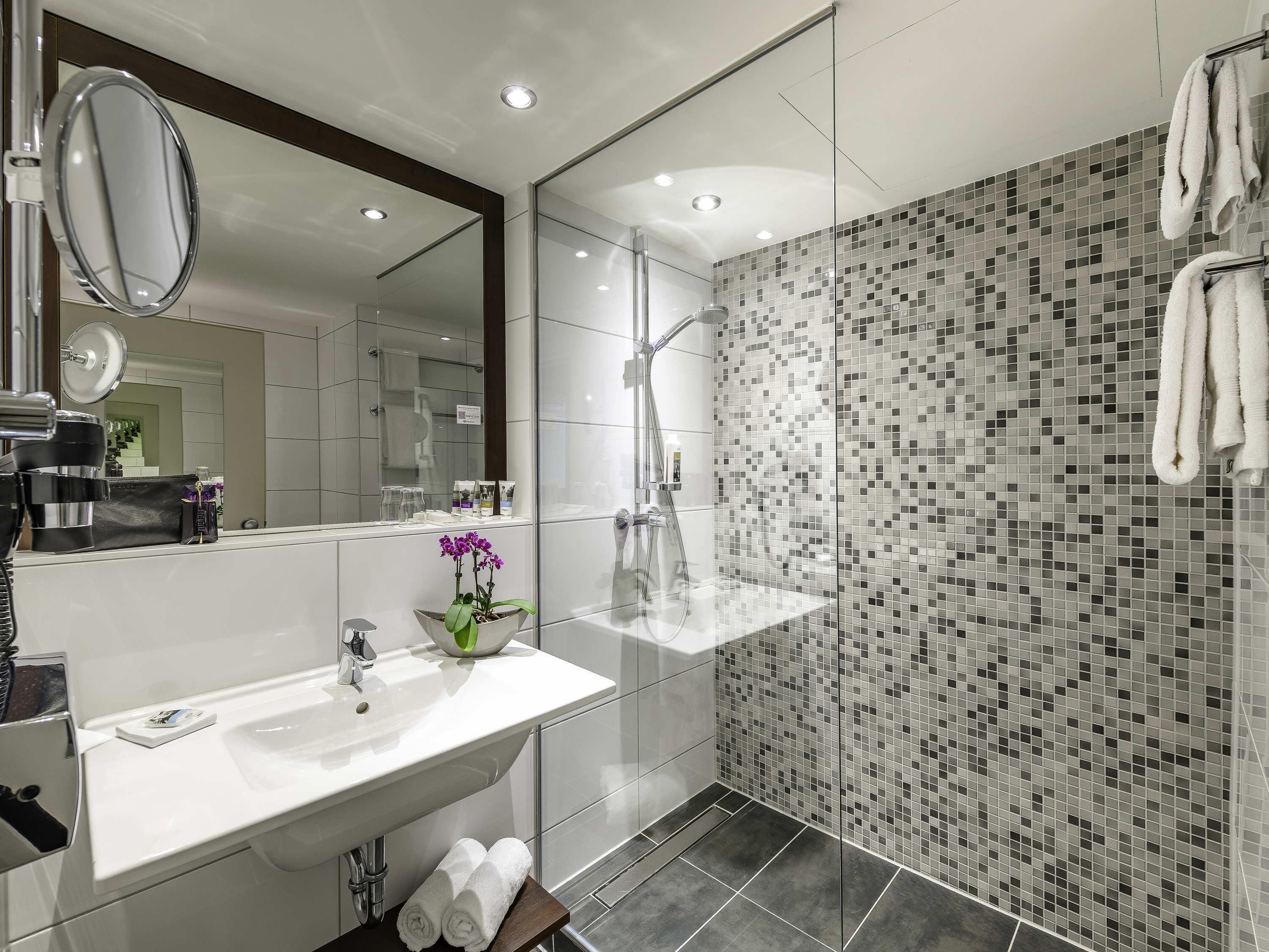 Un baño moderno con un espejo grande, un lavamanos y una zona de ducha.