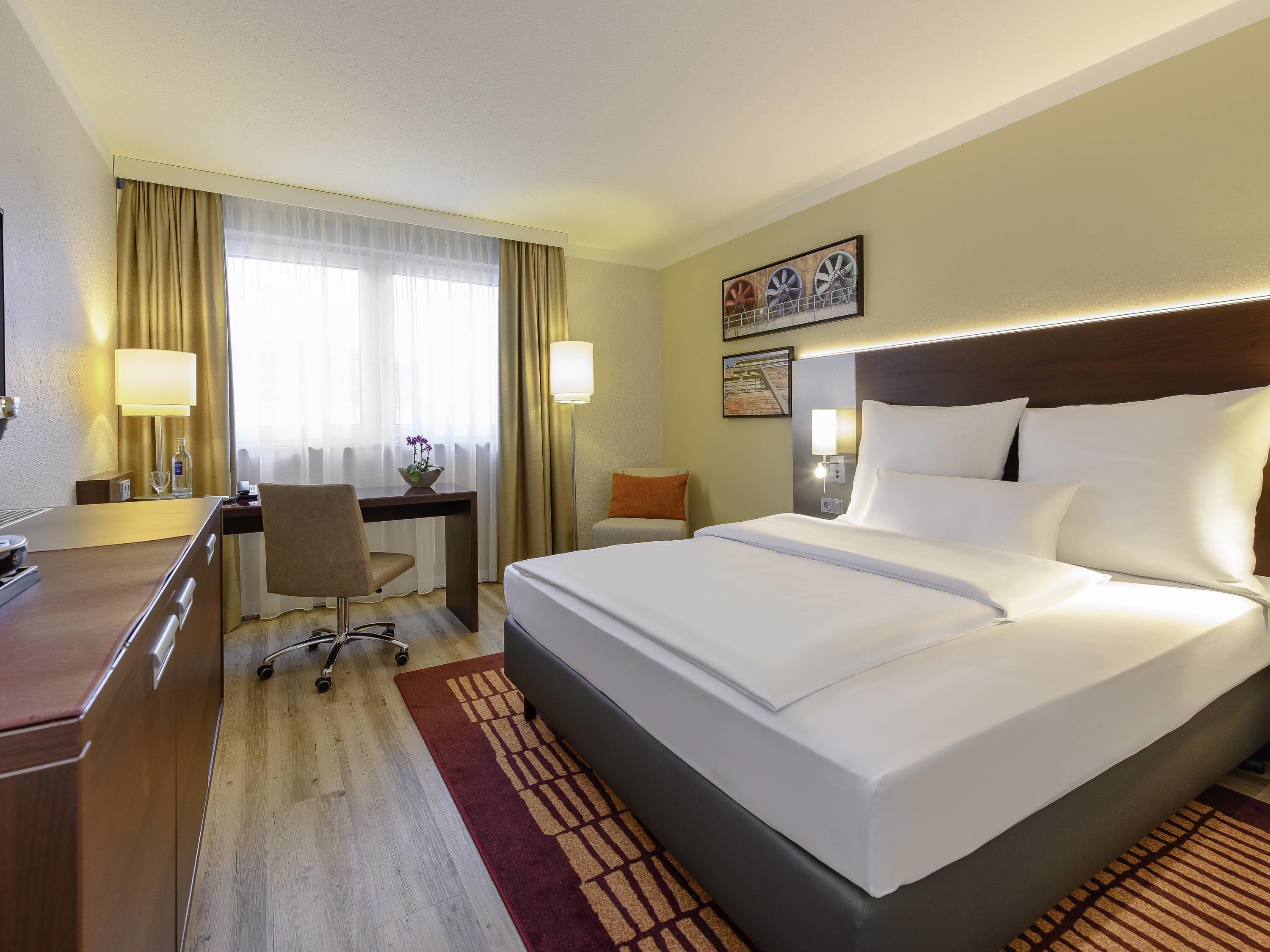 Ein Hotelzimmer mit Bett, Schreibtisch, Stuhl, Lampen und einem Bild an der Wand.