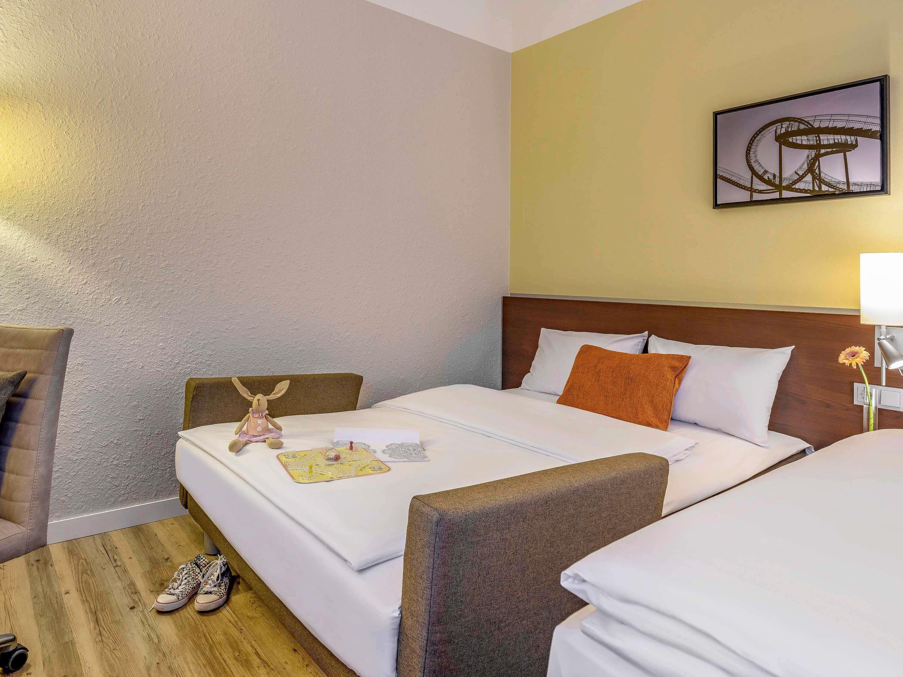 Ein Hotelzimmer mit zwei Betten, Holzboden, einem Wandbild und einem kleinen Tisch mit einer Karte und einer Flasche.