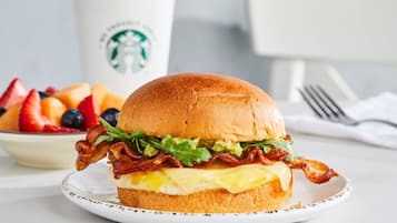 A breakfast sandwich on a plate with a Starbucks cup in the background.