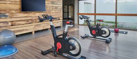 A modern gym with two stationary bikes, a large exercise ball, and a blue mat.