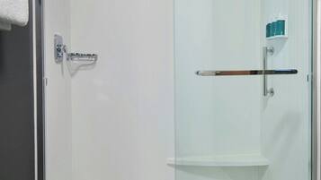 A glass-enclosed shower with a white door, a towel rack, and a small shelf with toiletries.
