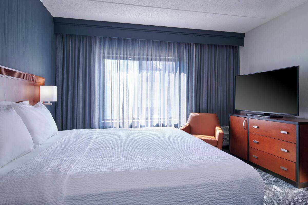 A hotel room with a large bed, a television, a desk, and a chair.