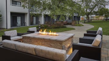 Un área de estar al aire libre con una chimenea, rodeada de muros de piedra y amueblada con sofás y sillones de mimbre.