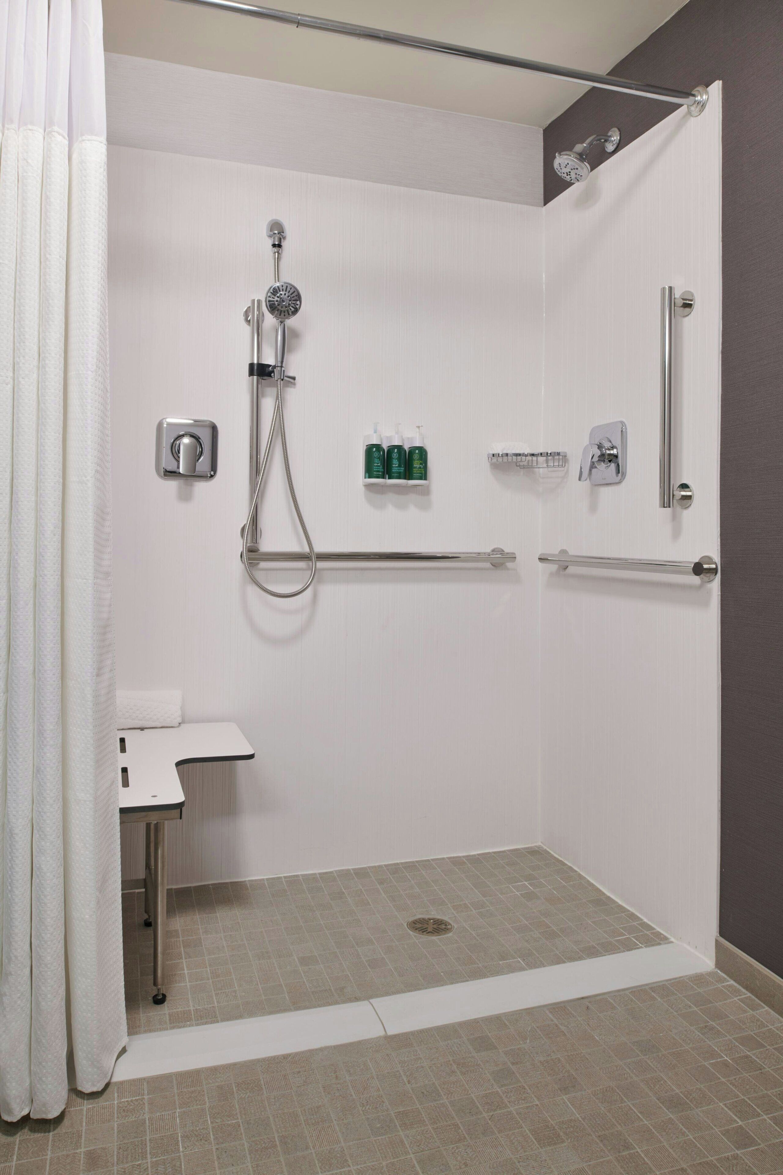 A walk-in shower with a grab bar, a small sink, and a showerhead.